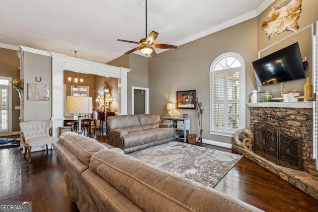 living room featuring a stone fireplace, wood-type flooring, crown molding, decorative columns, and ceiling fan with notable chandelier