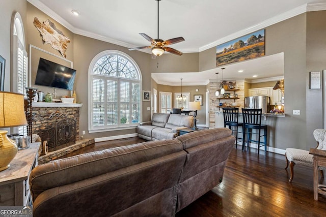 living room with ceiling fan with notable chandelier, ornamental molding, dark hardwood / wood-style flooring, and a stone fireplace