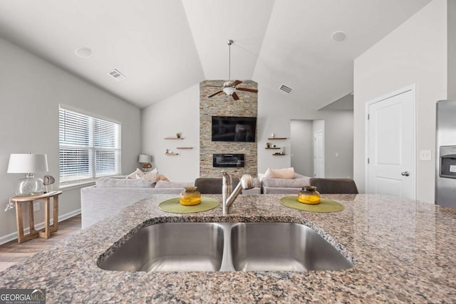 kitchen featuring vaulted ceiling, stone countertops, a fireplace, ceiling fan, and sink