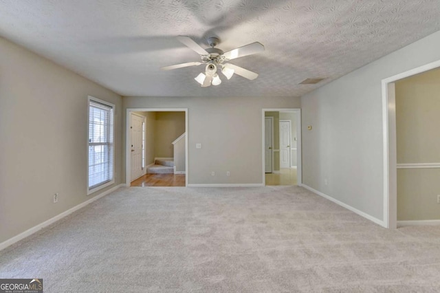 empty room featuring ceiling fan, light colored carpet, and a textured ceiling