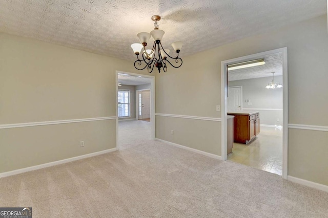 empty room featuring a textured ceiling, light carpet, and a chandelier