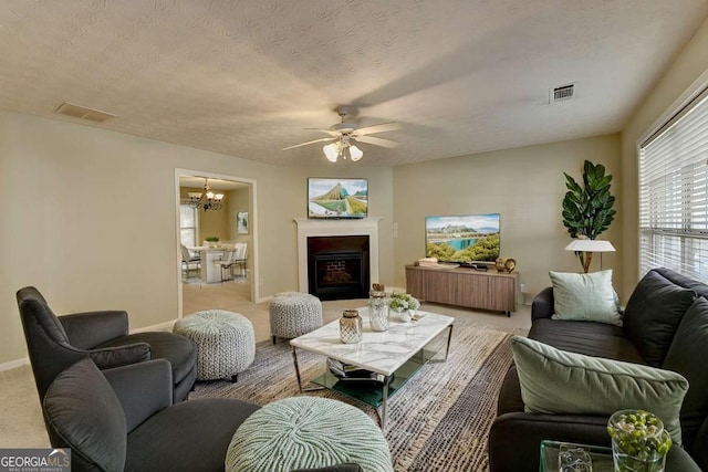 living room featuring a textured ceiling, light colored carpet, and ceiling fan with notable chandelier