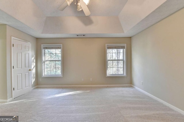 unfurnished room with a raised ceiling, light colored carpet, and ceiling fan