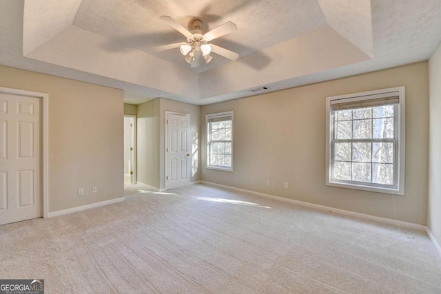 unfurnished bedroom featuring a raised ceiling, ceiling fan, a textured ceiling, and light carpet