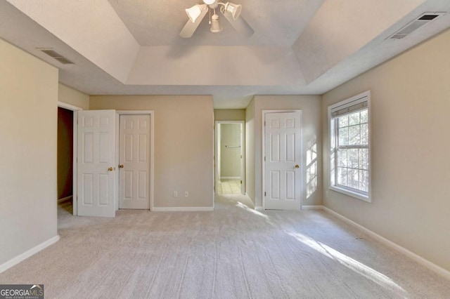 unfurnished bedroom with ceiling fan, a tray ceiling, and light carpet