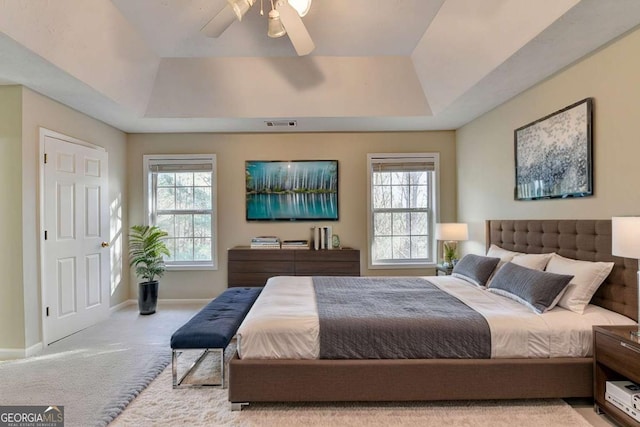 bedroom with light colored carpet, ceiling fan, and a tray ceiling