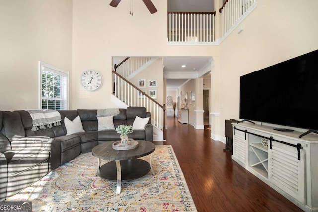 living room with a high ceiling, ceiling fan, ornamental molding, and dark wood-type flooring