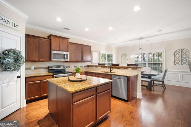 kitchen with stainless steel appliances, decorative light fixtures, a center island, and sink