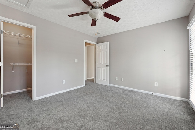 unfurnished bedroom featuring a textured ceiling, ceiling fan, a spacious closet, and carpet flooring