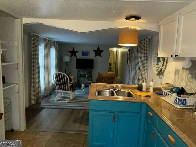 kitchen with white cabinets, a textured ceiling, blue cabinetry, and sink