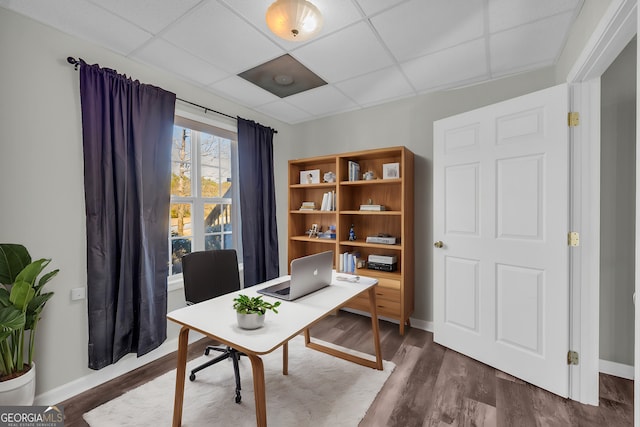 home office with dark hardwood / wood-style flooring and a paneled ceiling