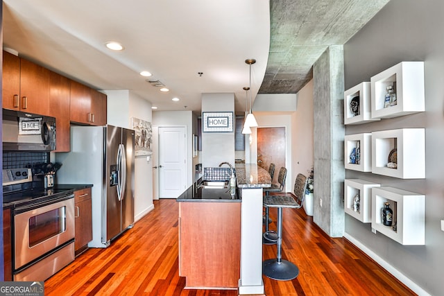 kitchen with stainless steel appliances, kitchen peninsula, a kitchen bar, sink, and decorative light fixtures