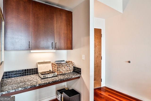 kitchen featuring built in desk, dark brown cabinetry, dark stone countertops, and dark hardwood / wood-style floors