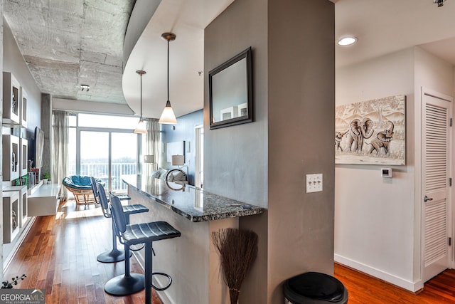 kitchen with kitchen peninsula, dark stone counters, hanging light fixtures, dark hardwood / wood-style flooring, and a breakfast bar