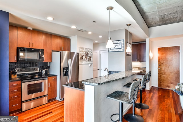 kitchen featuring a breakfast bar, stainless steel appliances, hardwood / wood-style floors, and pendant lighting