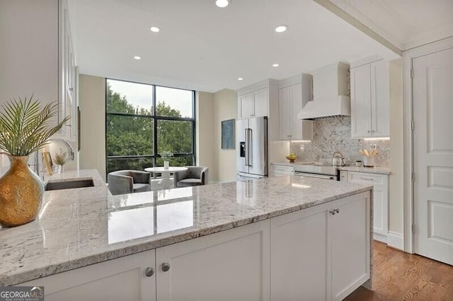 kitchen with stainless steel appliances, sink, white cabinetry, wall chimney exhaust hood, and light stone countertops