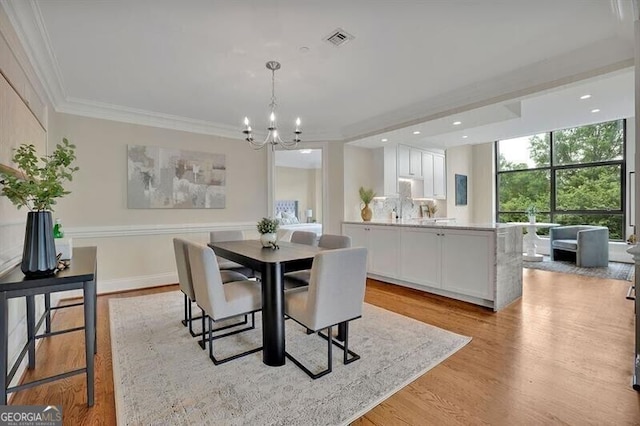 dining area featuring light hardwood / wood-style floors, ornamental molding, and an inviting chandelier