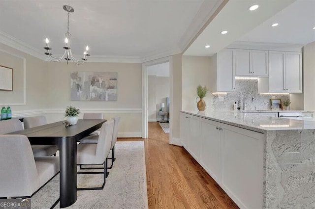 dining area with an inviting chandelier, ornamental molding, light hardwood / wood-style flooring, and sink