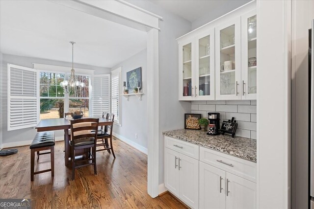 bar with stainless steel refrigerator with ice dispenser, white cabinets, decorative backsplash, and light stone countertops