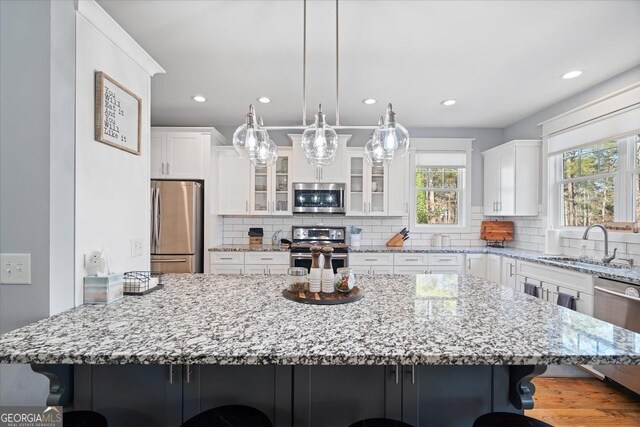 kitchen with white cabinets, stainless steel appliances, pendant lighting, a kitchen bar, and sink