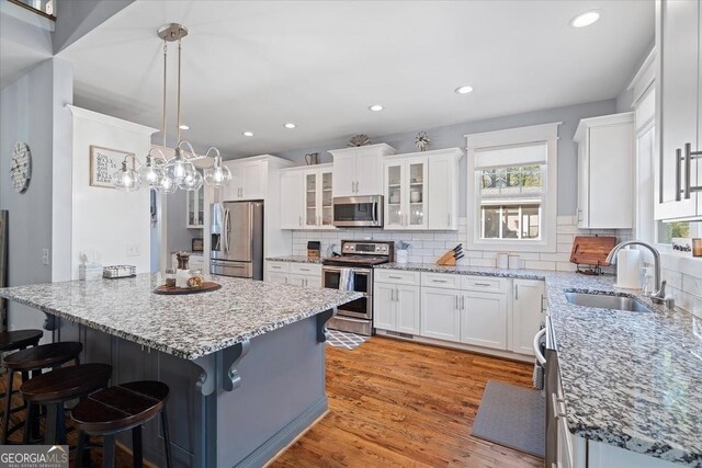 kitchen with white cabinets, a breakfast bar area, decorative backsplash, pendant lighting, and appliances with stainless steel finishes