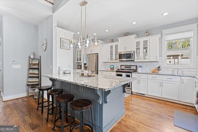 kitchen with decorative light fixtures, white cabinetry, tasteful backsplash, light stone countertops, and appliances with stainless steel finishes