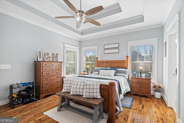 bedroom featuring ceiling fan, a raised ceiling, ensuite bath, and hardwood / wood-style flooring