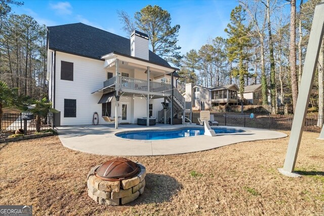 back of property with an outdoor fire pit, a balcony, a fenced in pool, and a patio