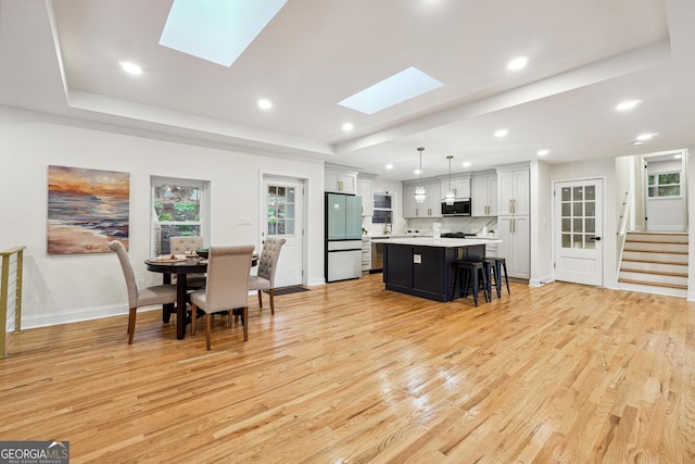 kitchen featuring white cabinets, a center island, hanging light fixtures, refrigerator, and a raised ceiling