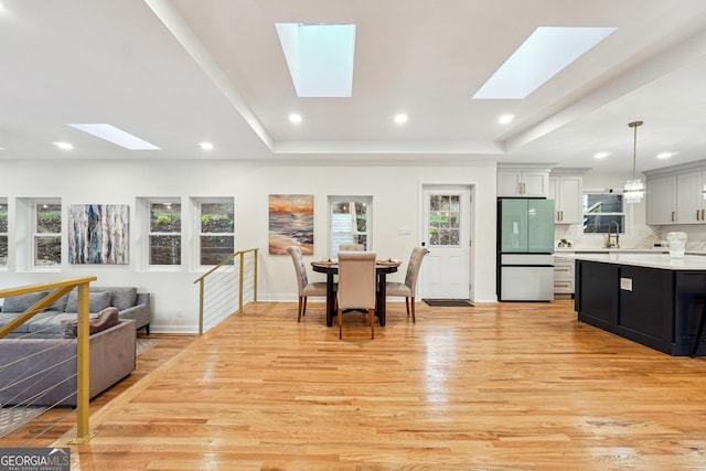 interior space with a skylight, a tray ceiling, decorative light fixtures, refrigerator, and light hardwood / wood-style flooring