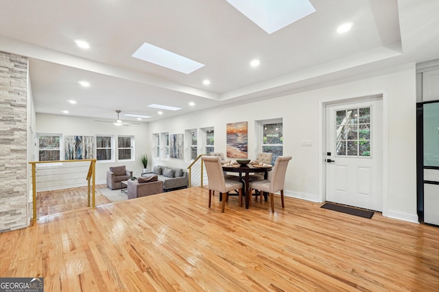 dining space featuring light hardwood / wood-style floors, a tray ceiling, and a skylight