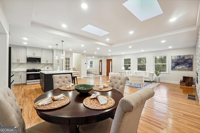 dining space with a skylight, a tray ceiling, and light hardwood / wood-style floors