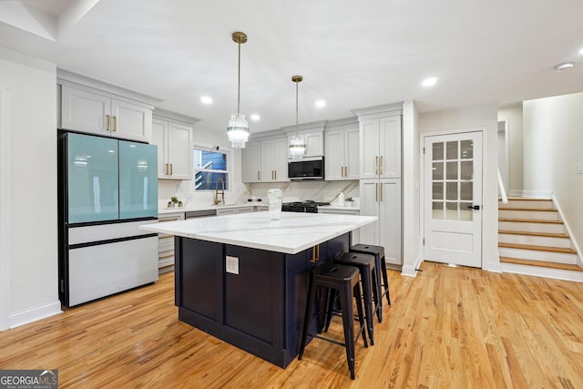 kitchen featuring pendant lighting, a center island, tasteful backsplash, fridge, and light hardwood / wood-style flooring