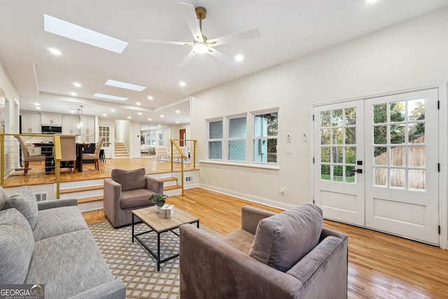 living room with french doors, ceiling fan, a skylight, and light hardwood / wood-style flooring