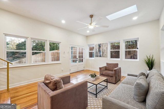 living room with ceiling fan, a skylight, and light hardwood / wood-style flooring