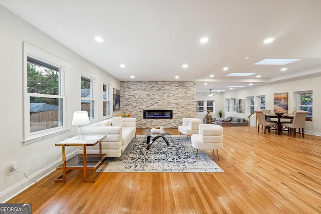 living room with light wood-type flooring, a skylight, and a fireplace