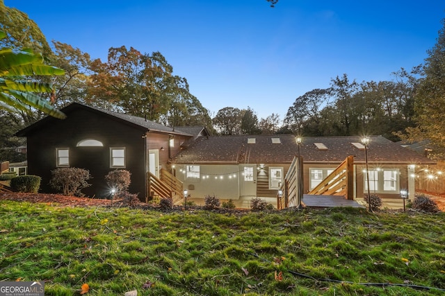 back house at dusk featuring a lawn