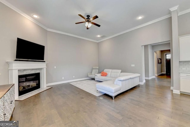 living room with a high end fireplace, hardwood / wood-style floors, ceiling fan, and crown molding