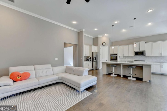 living room featuring light wood-type flooring, ceiling fan, crown molding, and sink