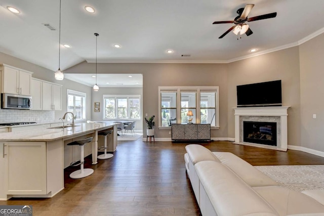 living room featuring dark wood-type flooring, vaulted ceiling, a premium fireplace, ceiling fan, and sink