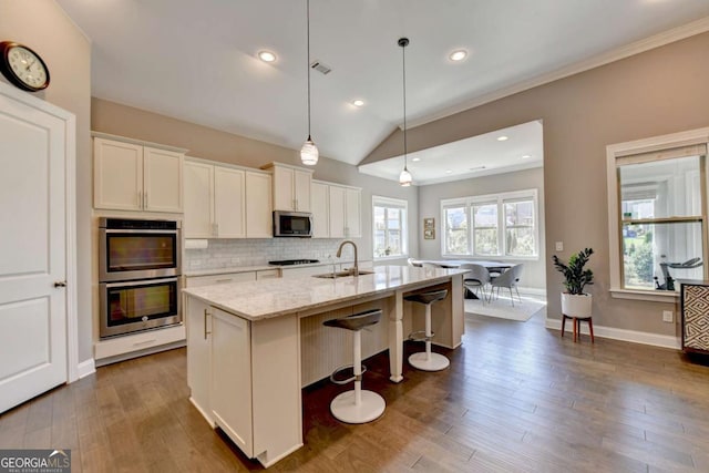 kitchen featuring white cabinets, a center island with sink, appliances with stainless steel finishes, and hanging light fixtures