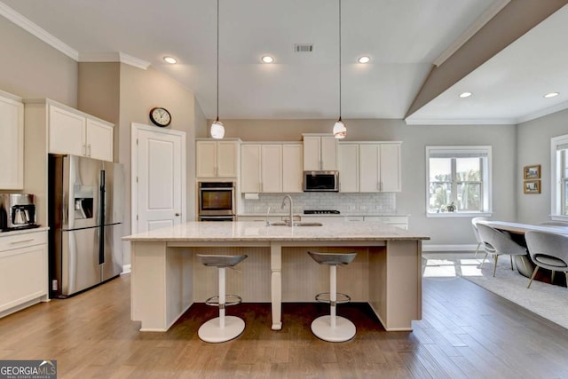 kitchen with light stone countertops, vaulted ceiling, hanging light fixtures, stainless steel appliances, and a kitchen island with sink