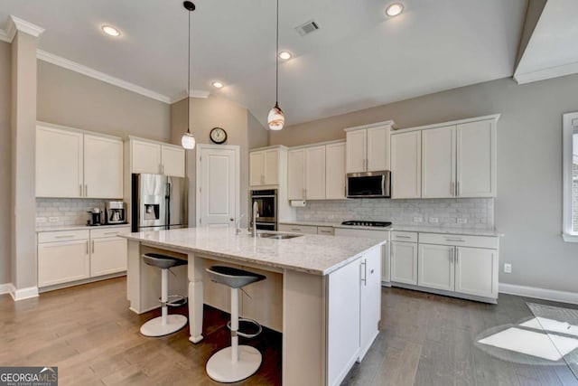 kitchen with white cabinets, stainless steel appliances, a center island with sink, and hanging light fixtures