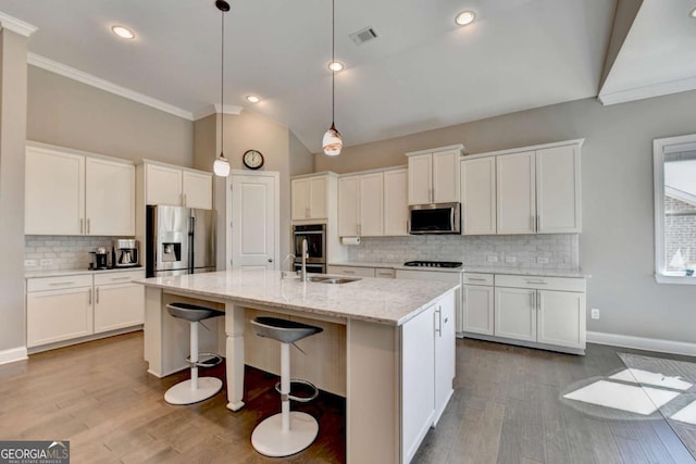 kitchen featuring stainless steel appliances, white cabinets, light stone countertops, a center island with sink, and pendant lighting