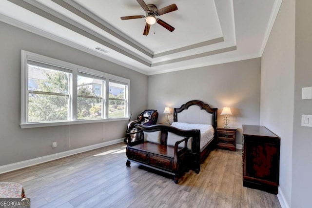 bedroom featuring ceiling fan, a tray ceiling, ornamental molding, and light hardwood / wood-style flooring