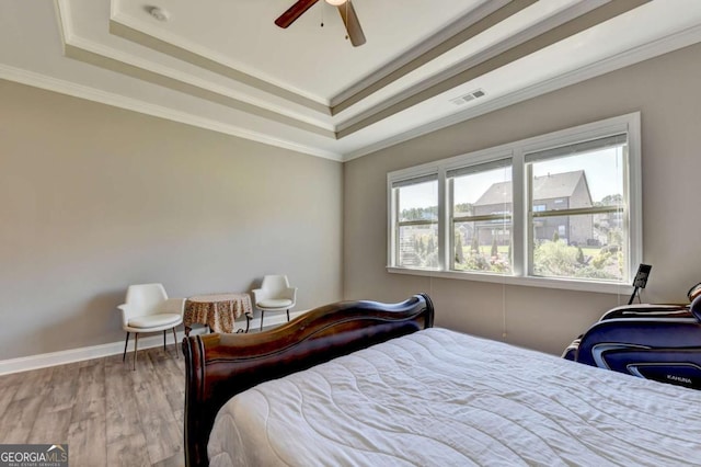 bedroom with ceiling fan, ornamental molding, hardwood / wood-style floors, and a tray ceiling