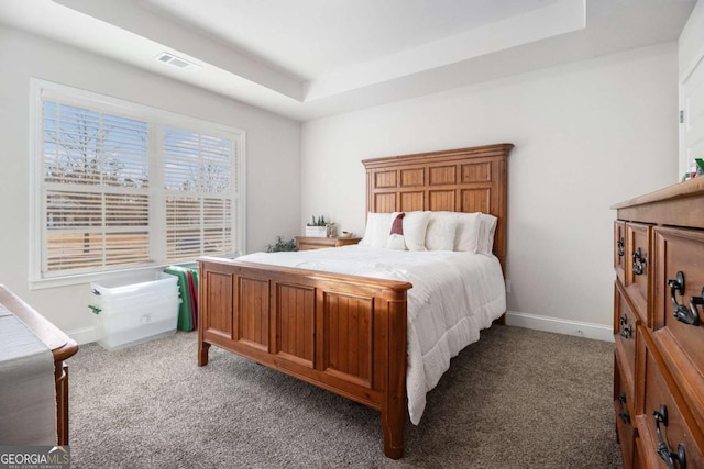 bedroom with a raised ceiling and dark colored carpet