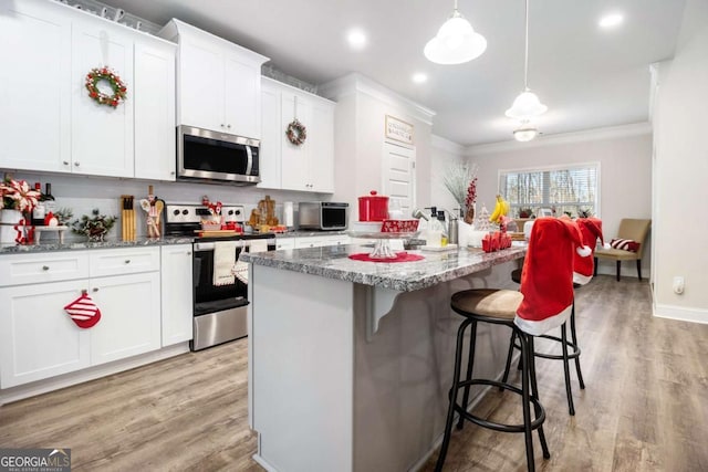 kitchen with decorative light fixtures, white cabinets, light wood-type flooring, an island with sink, and appliances with stainless steel finishes