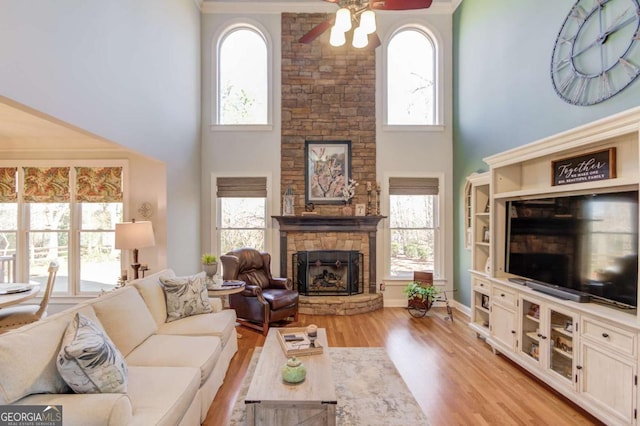 living room with a towering ceiling, ceiling fan, light wood-type flooring, and a stone fireplace