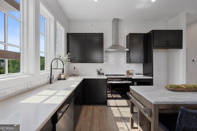 kitchen featuring appliances with stainless steel finishes, light hardwood / wood-style floors, decorative backsplash, wall chimney exhaust hood, and sink